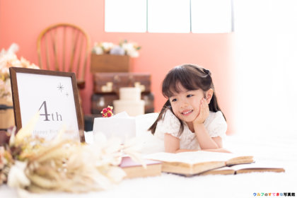 北摂吹田にあるフォトスタジオで、4歳のお誕生日記念の女の子が、うつ伏せに寝転んで、頬杖しながら、優しい笑顔でケーキを見つめている写真。